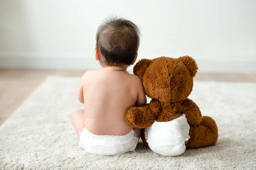 Младенец сидит спиной вместе с плюшевой игрушкой