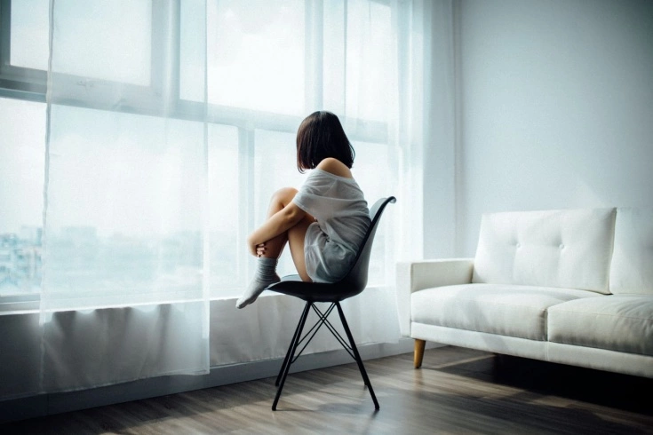 Девушка меланхолично сидит в кресле в собственной комнате