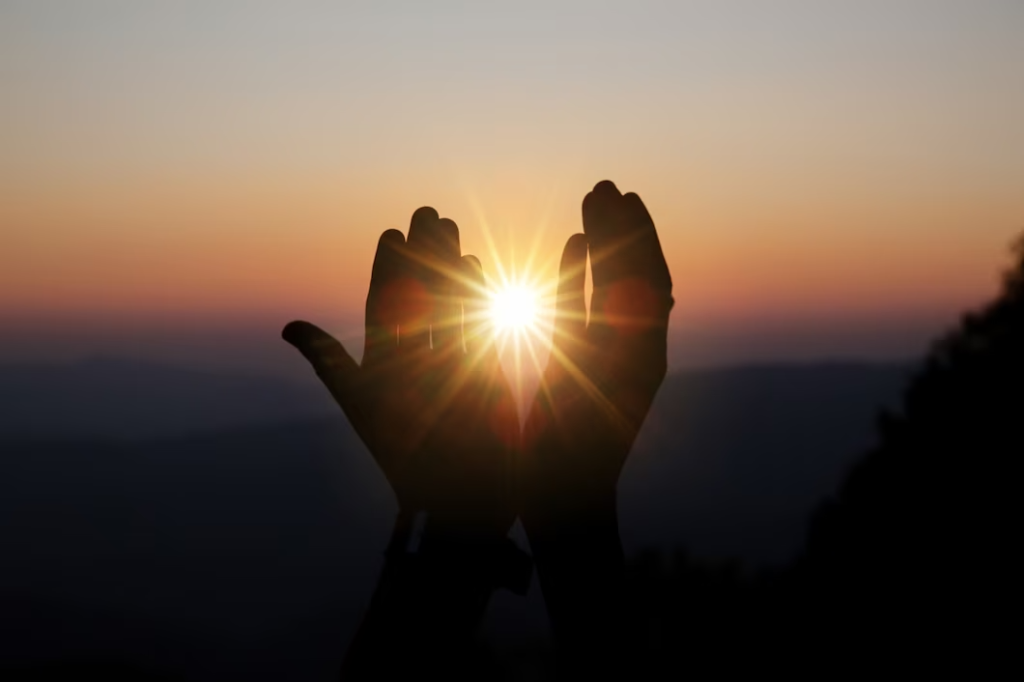 Человек протягивает руку к солнцу на закате